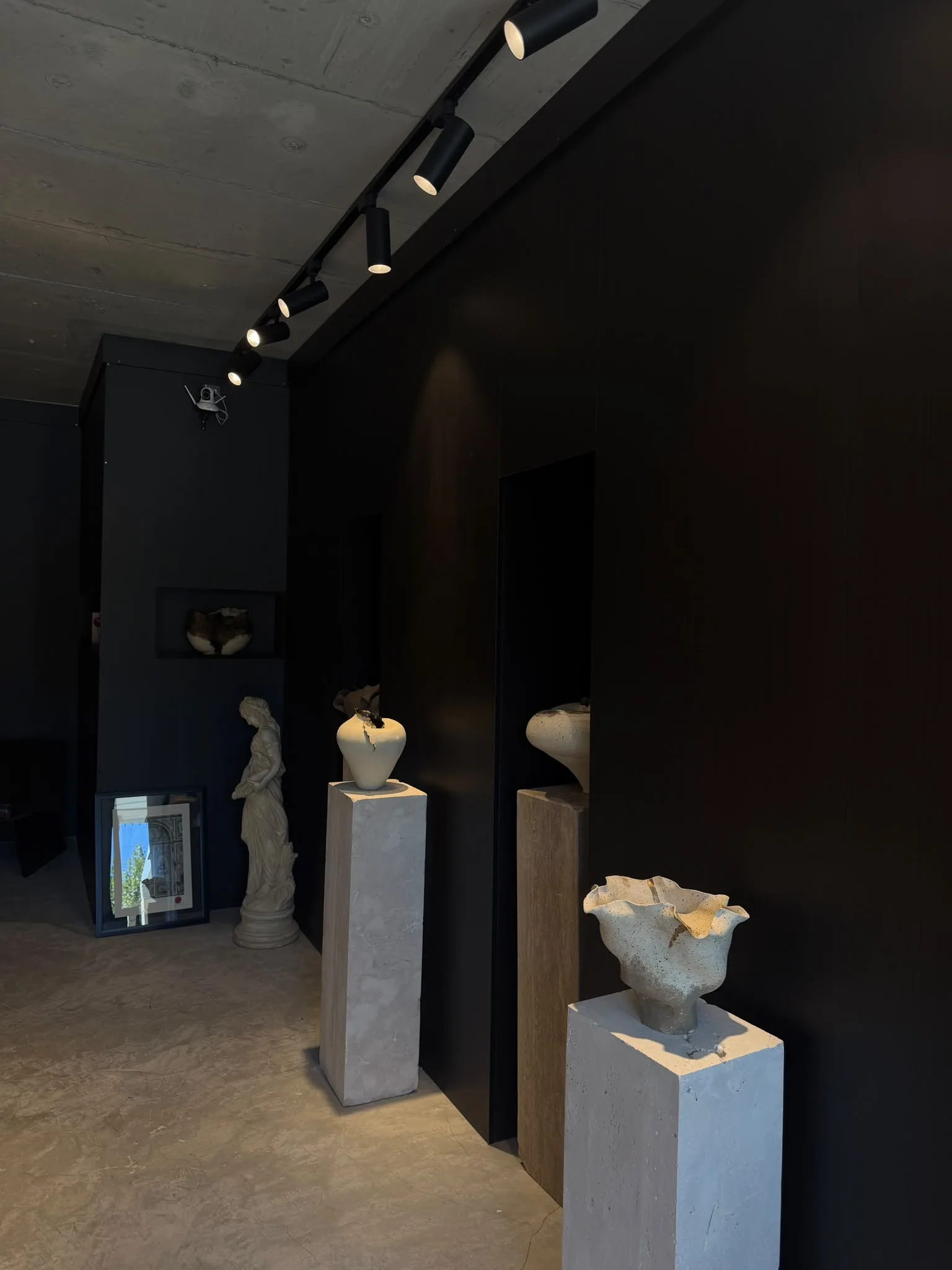 A dark-walled corridor: ceramics on plinths under track lights, a plaster figure beyond