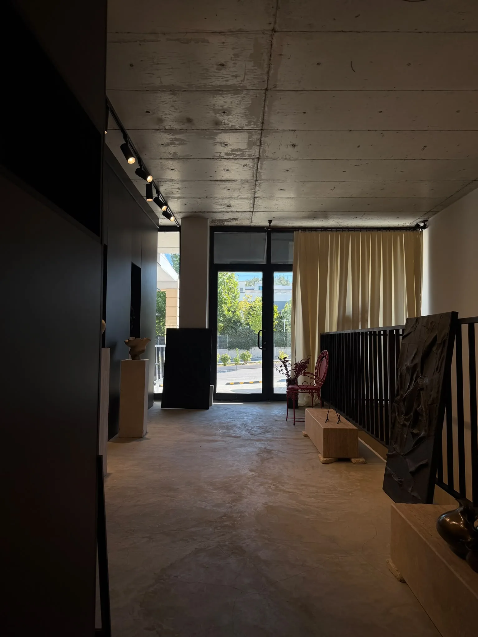 The concrete-ceilinged room opening toward glass doors and the garden, plinths and a large relief panel along the side