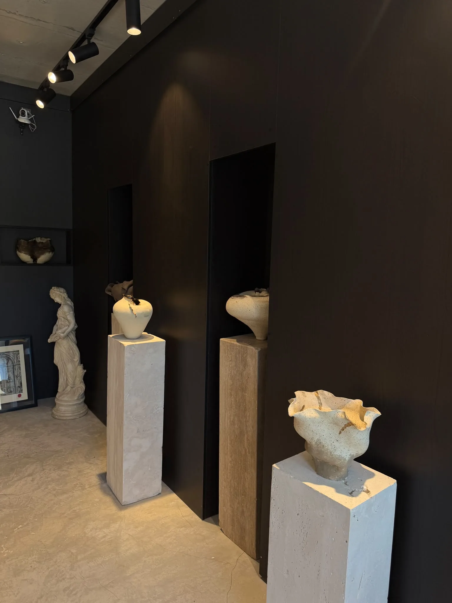 Three ceramic pieces on plinths, spotlit in front of black wall niches